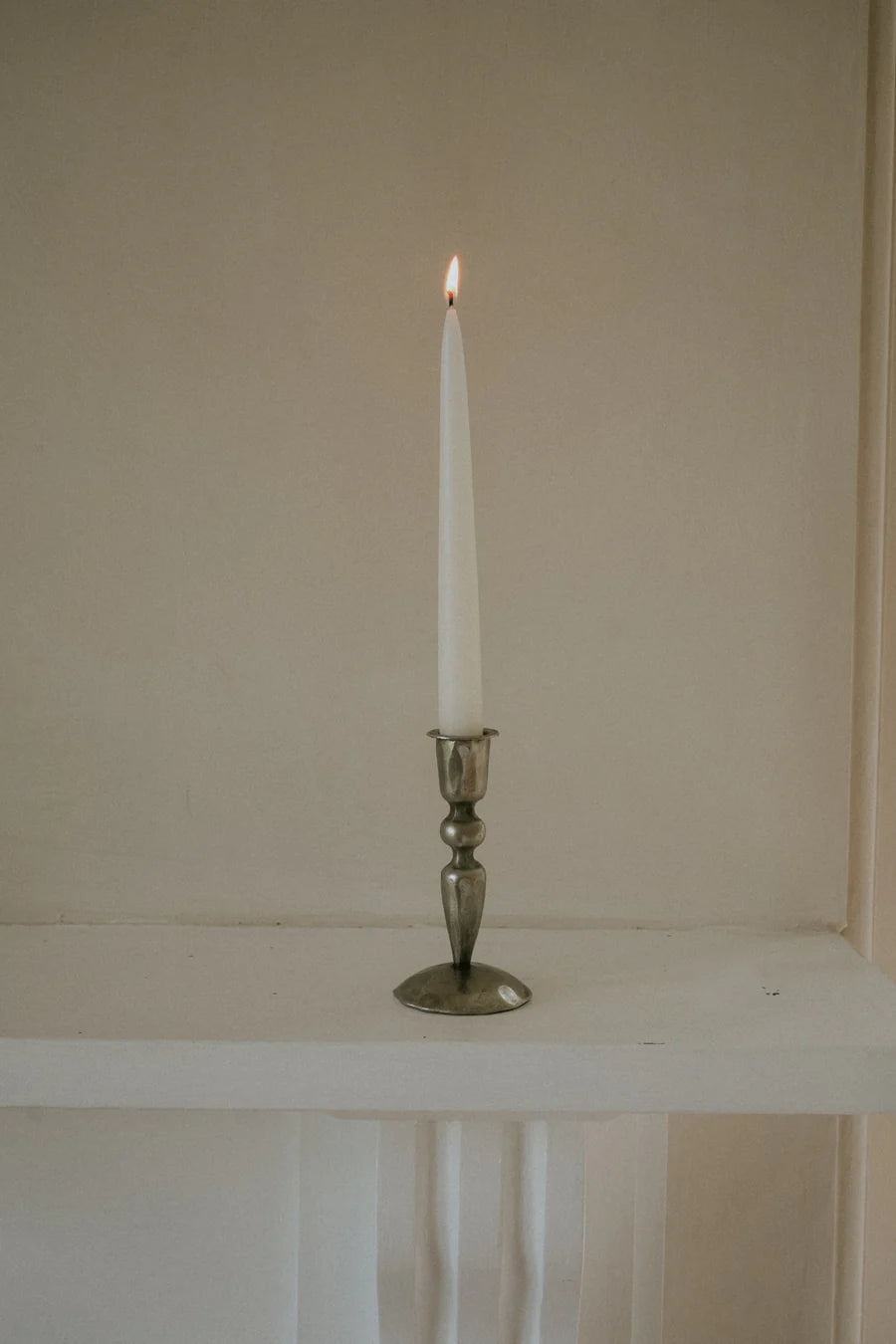White candle in a silver holder on a white surface with a neutral background