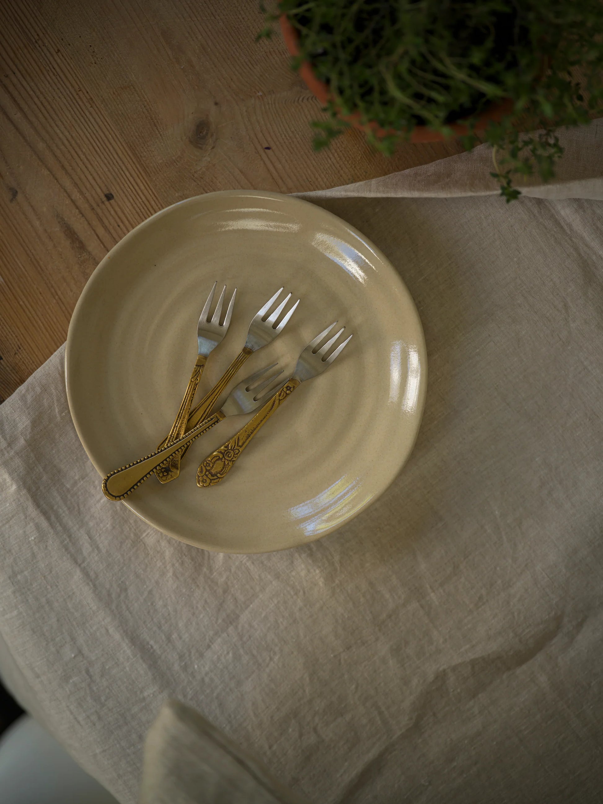 Set of gold forks on a beige plate with a white cloth and plant in the background