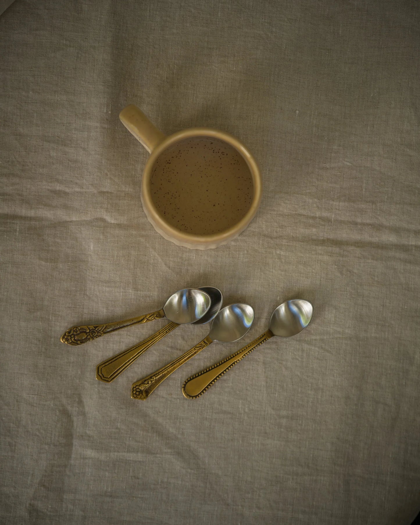 Ceramic mug and vintage spoons on a textured fabric surface