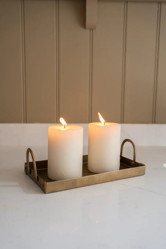 Two white candles in a brass holder on a white surface with a beige wall background