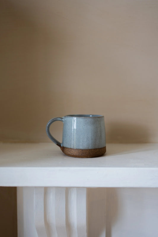 Blue ceramic mug with brown base on a white surface against a beige wall