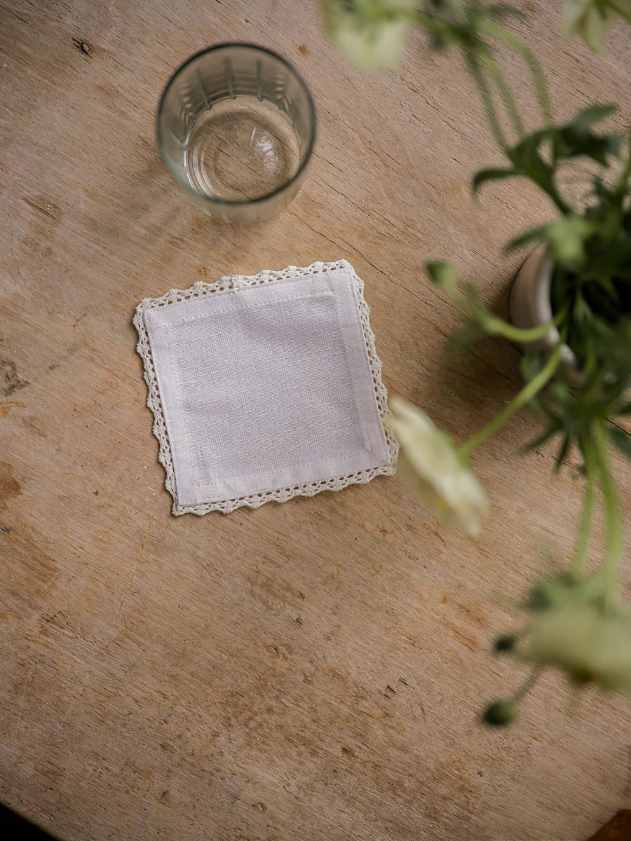 White doily on a wooden surface with a glass of water and flowers.