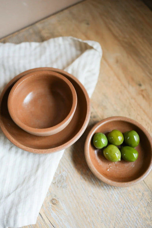 Two terracotta bowls on a wooden surface with one containing green grapes.