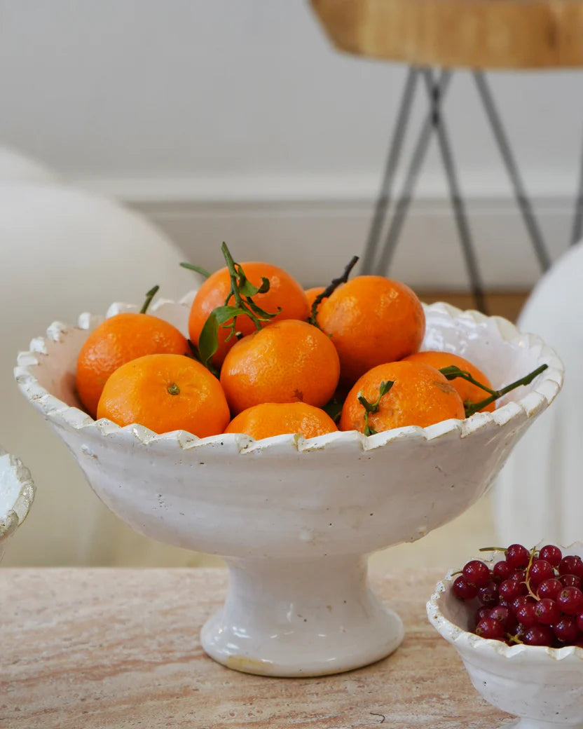 White decorative bowl filled with oranges on a wooden surface