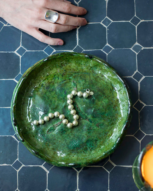 Green ceramic plate with a necklace on a blue tiled surface
