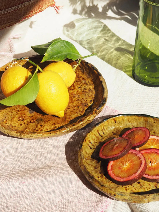 Two ceramic plates with lemons and sliced fruit on a textured surface.