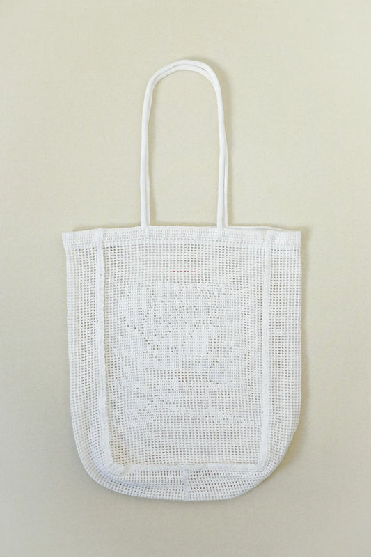 A white open crochet tote bag with long handles, shown flat against a light beige background.