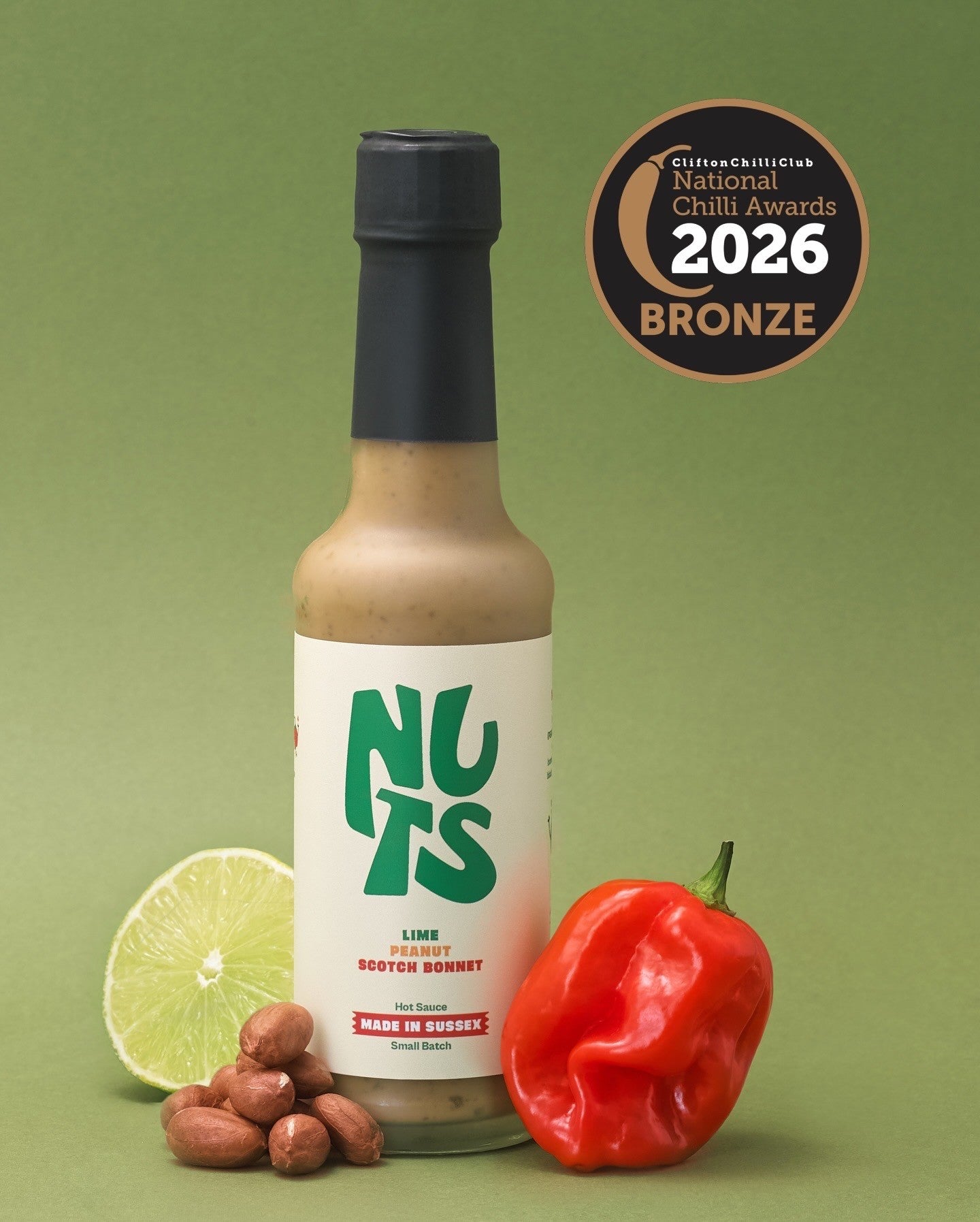 Hot sauce bottle labeled 'NUTS' with chili, lime, and nuts on a green background