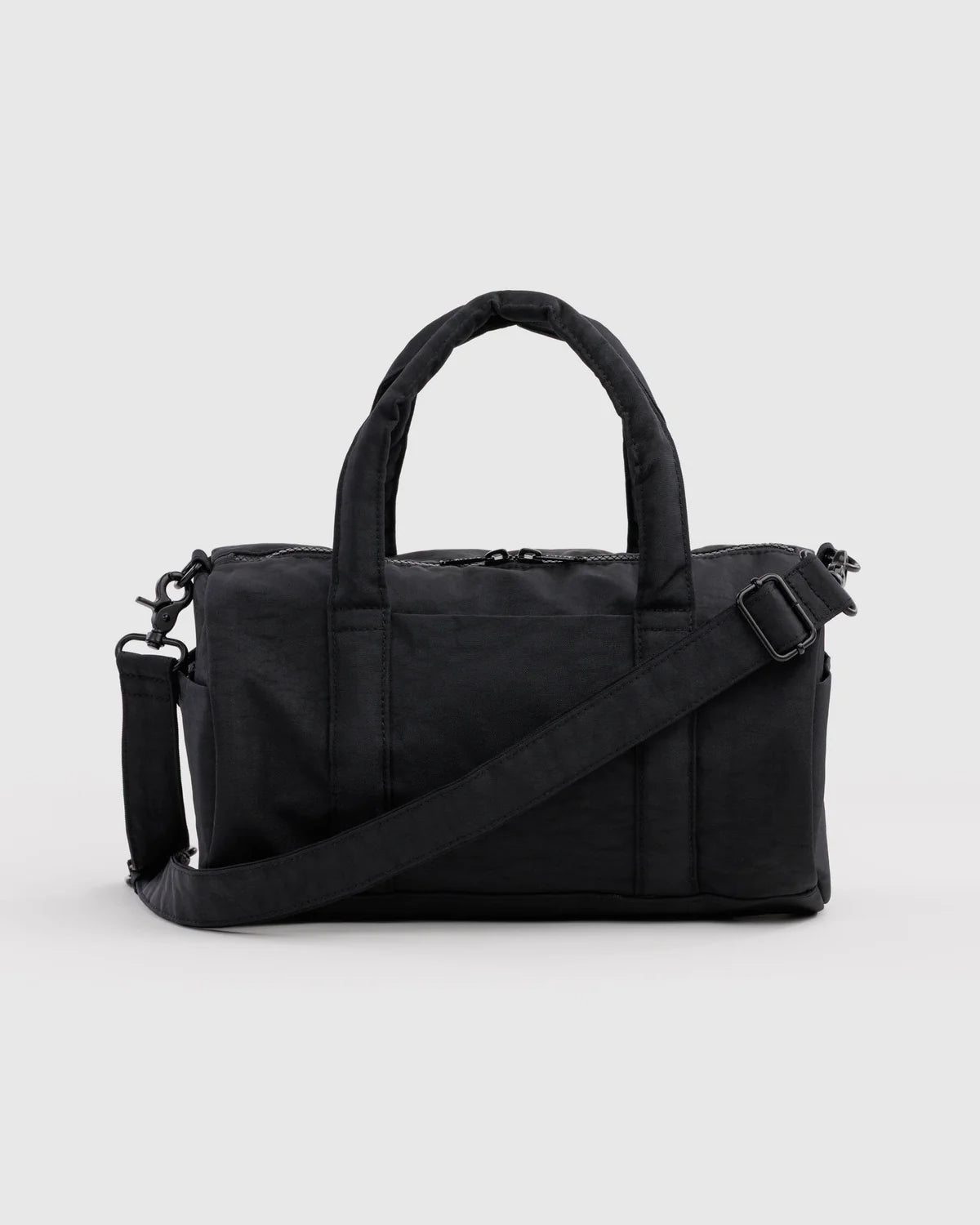 A black nylon duffel bag with dual top handles and an adjustable shoulder strap, shown against a light gray studio background.
