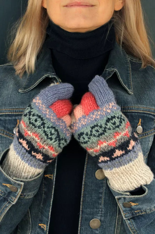 Person wearing a denim jacket and colorful knitted mittens with a dark background