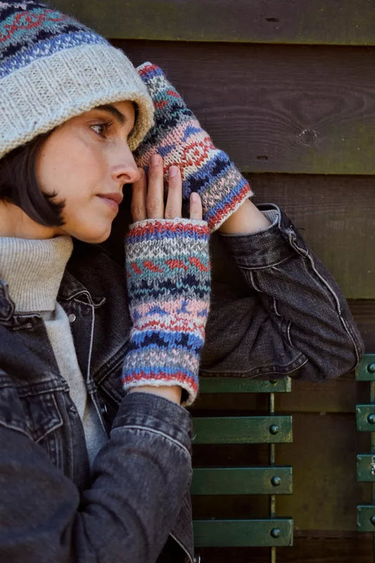 Person wearing a knitted hat and gloves against a wooden wall.