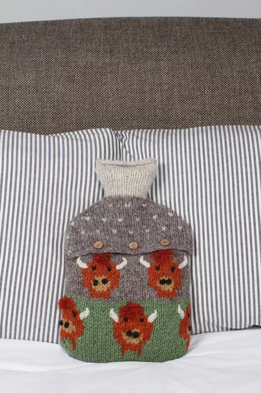 Knitted hot water bottle cover with bull design on a striped pillow