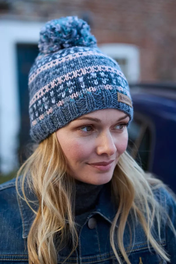 Woman wearing a blue knitted beanie with a pom-pom, standing outdoors.