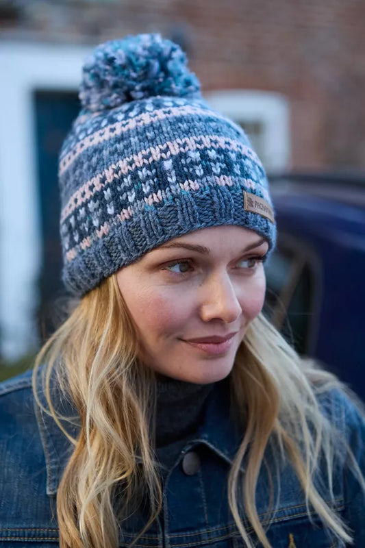 Woman wearing a blue knitted beanie with a pom-pom, standing outdoors.