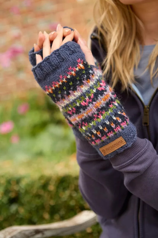 Person wearing a dark blue knitted fingerless glove with colorful pattern, held in front of a blurred natural background.