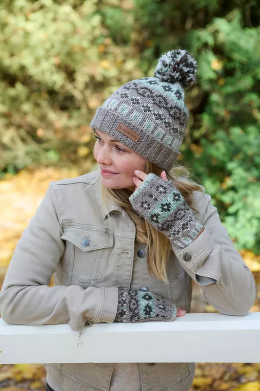 Person wearing a patterned knit hat and mittens outdoors with greenery in the background