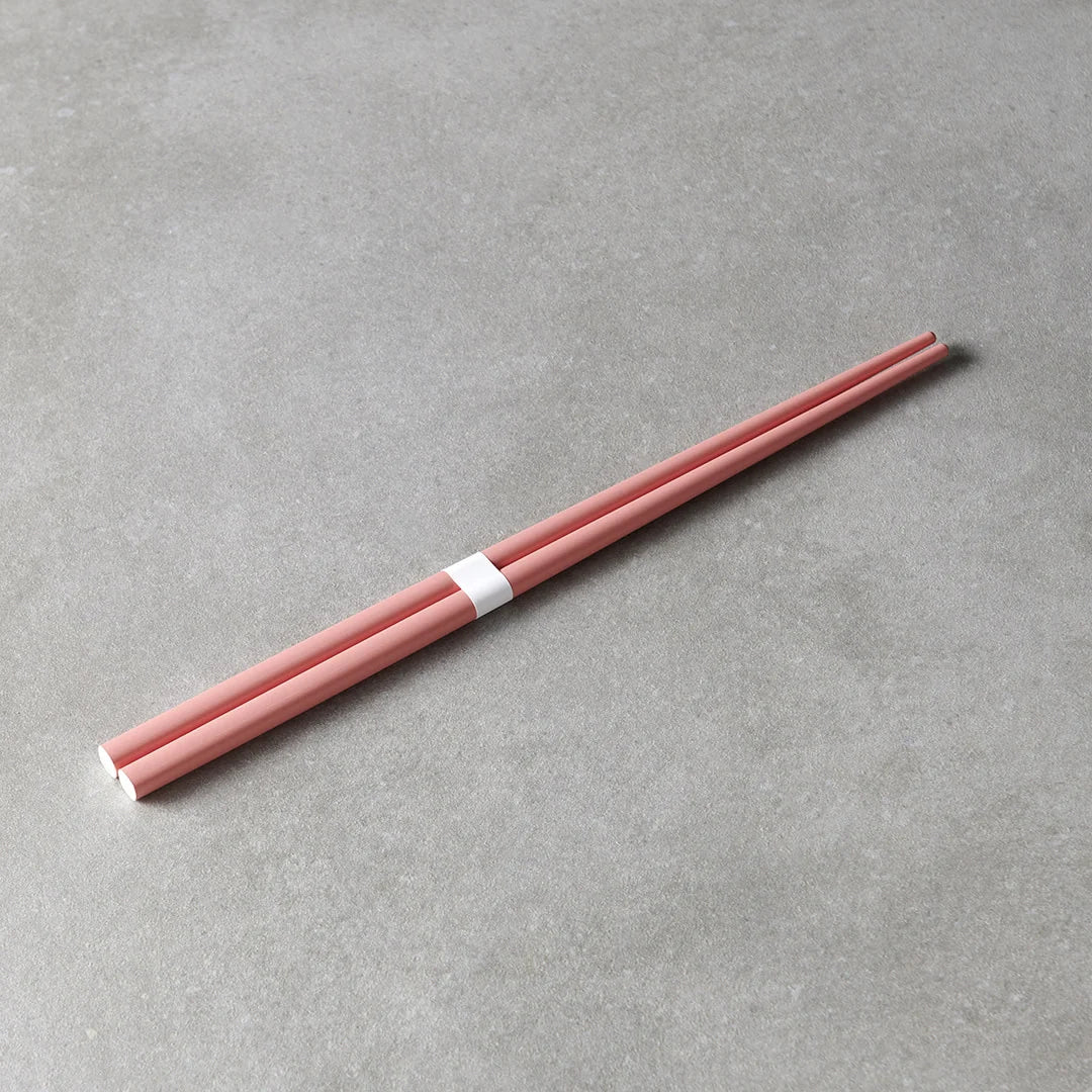 A pair of light pink chopsticks held together by a white paper band, placed diagonally on a textured gray surface.