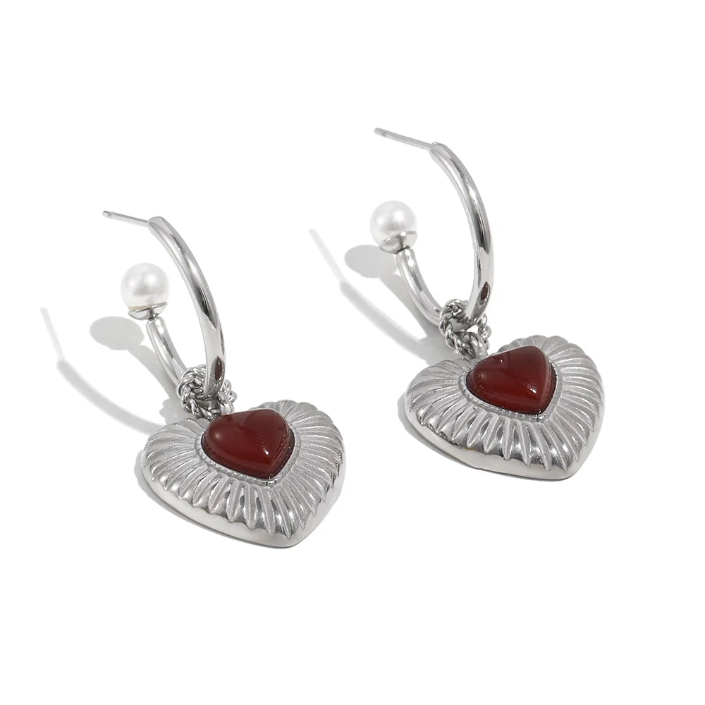 Heart-shaped earrings with red stones and pearl accents on a white background