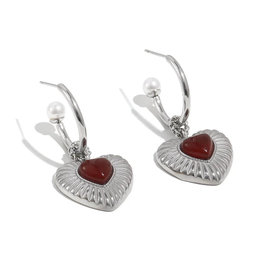 Heart-shaped earrings with red stones and pearl accents on a white background