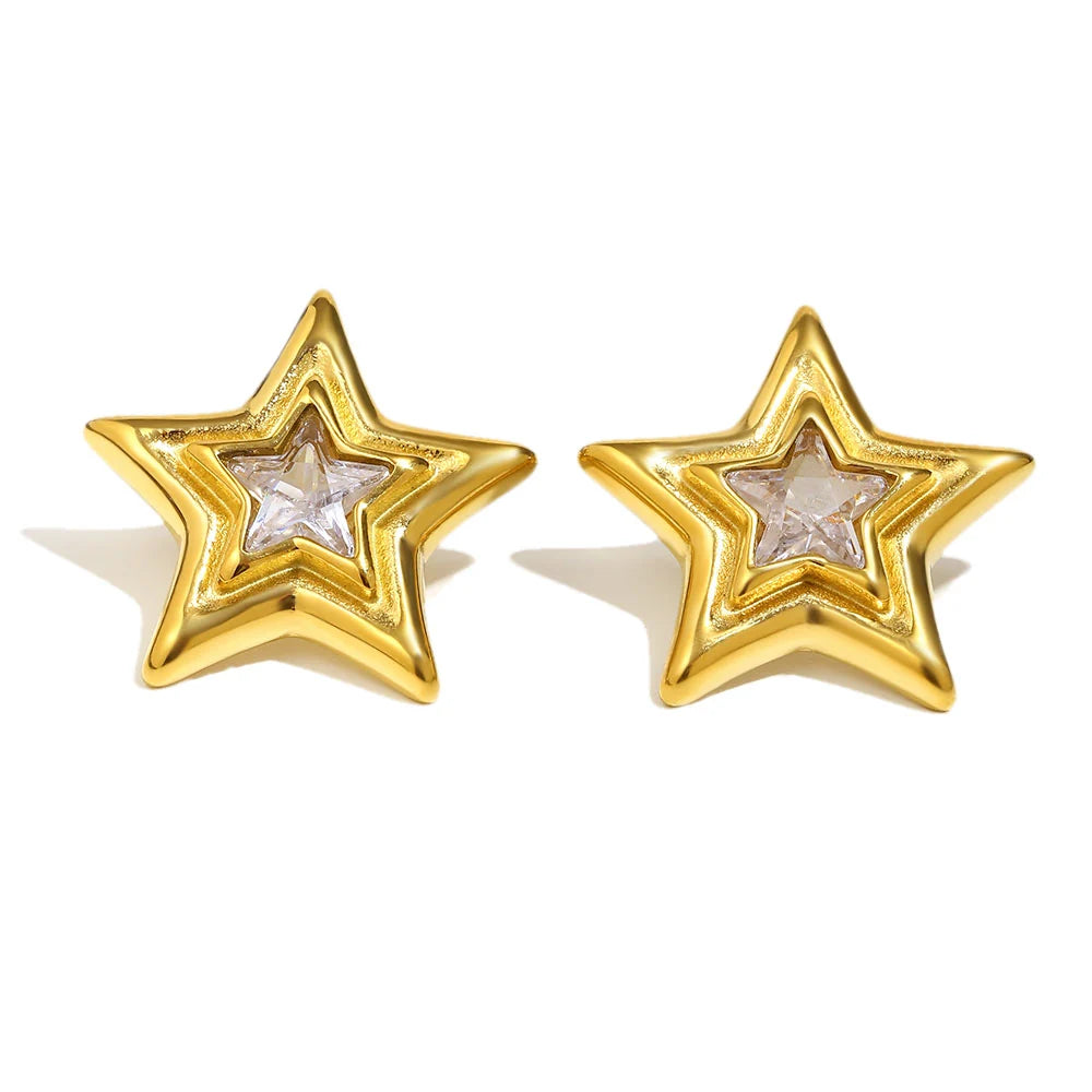 A pair of gold star-shaped stud earrings with a clear faceted crystal in the center, set against a plain white background.