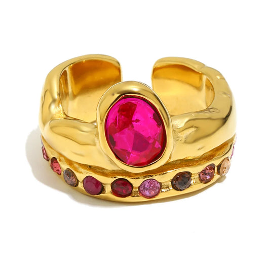 A gold-toned adjustable ring featuring a large oval-cut bright pink gemstone in the center and a row of smaller pink, purple, and red accent stones along the front, set against a plain white background.