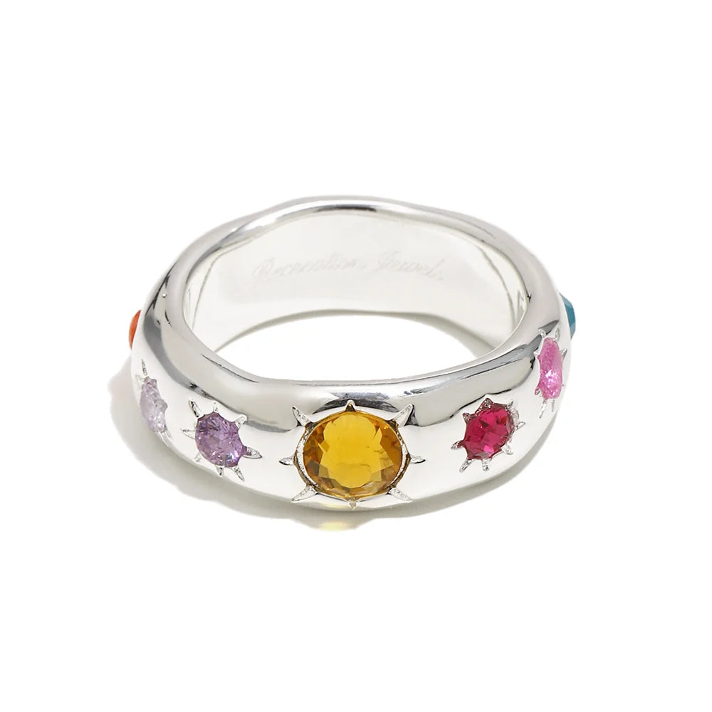 A sterling silver band ring featuring a central round yellow gemstone surrounded by smaller multicolored gemstones, shown on a white background.
