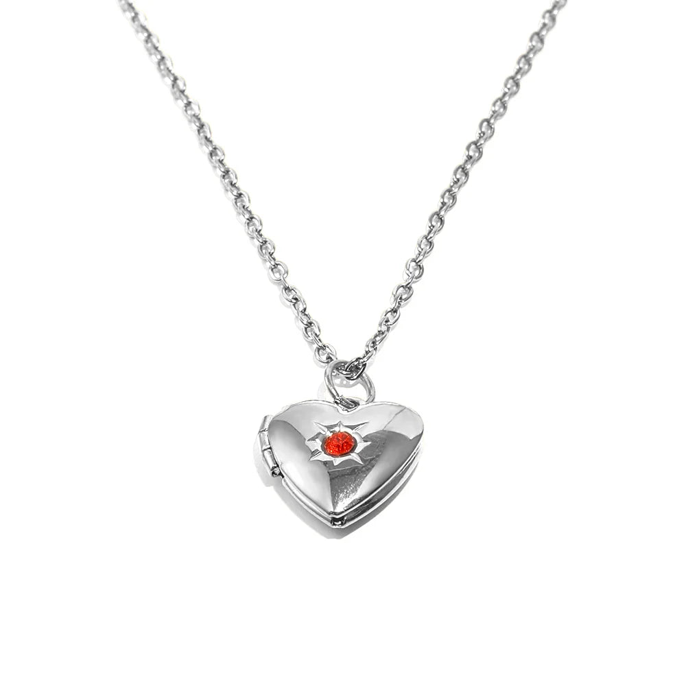 A silver heart-shaped locket pendant necklace with a small red heart in the center, suspended from a delicate silver chain against a plain white background.