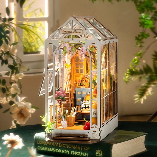 Miniature model of a garden house with indoor plants and decor, placed on a book.
