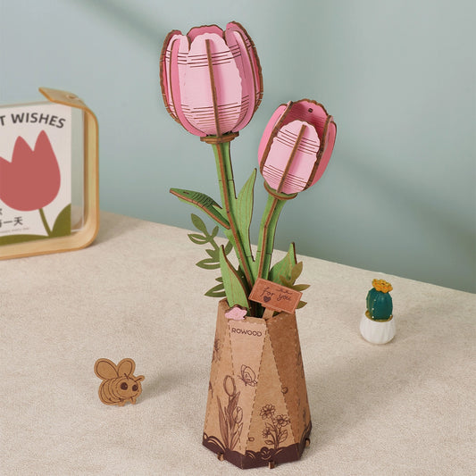 Cardboard tulips in a vase on a neutral surface with a light green wall in the background.
