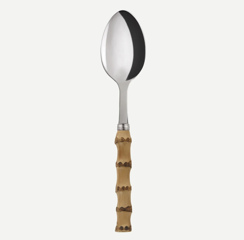 A stainless steel spoon with a decorative light brown bamboo handle, shown vertically against a plain off-white background.