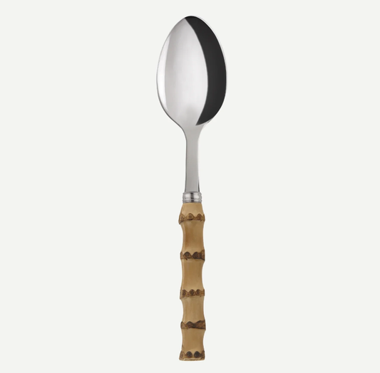 A stainless steel spoon with a decorative light brown bamboo handle, shown vertically against a plain off-white background.