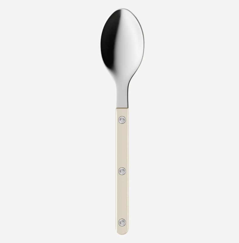 A modern stainless steel spoon with a cream-colored handle featuring three decorative silver rivets, shown against a light gray background.