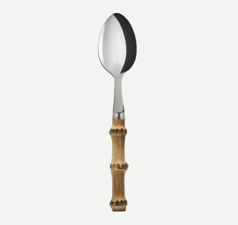 A stainless steel serving spoon with a decorative bamboo handle, shown vertically against a light gray background.