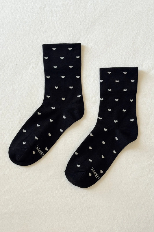 Pair of black socks with white heart patterns on a light beige background
