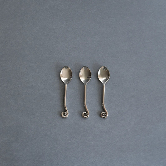 Three small silver spoons with decorative curled handles, arranged side by side on a textured gray background.