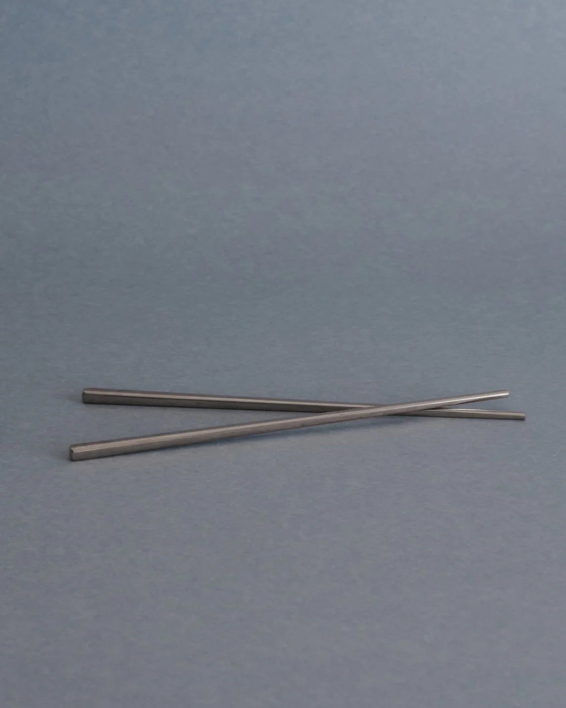 Two slim metallic rods or chopsticks crossed on a plain gray background.