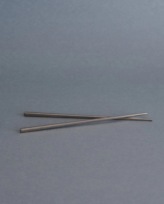Two slim metallic rods or chopsticks crossed on a plain gray background.