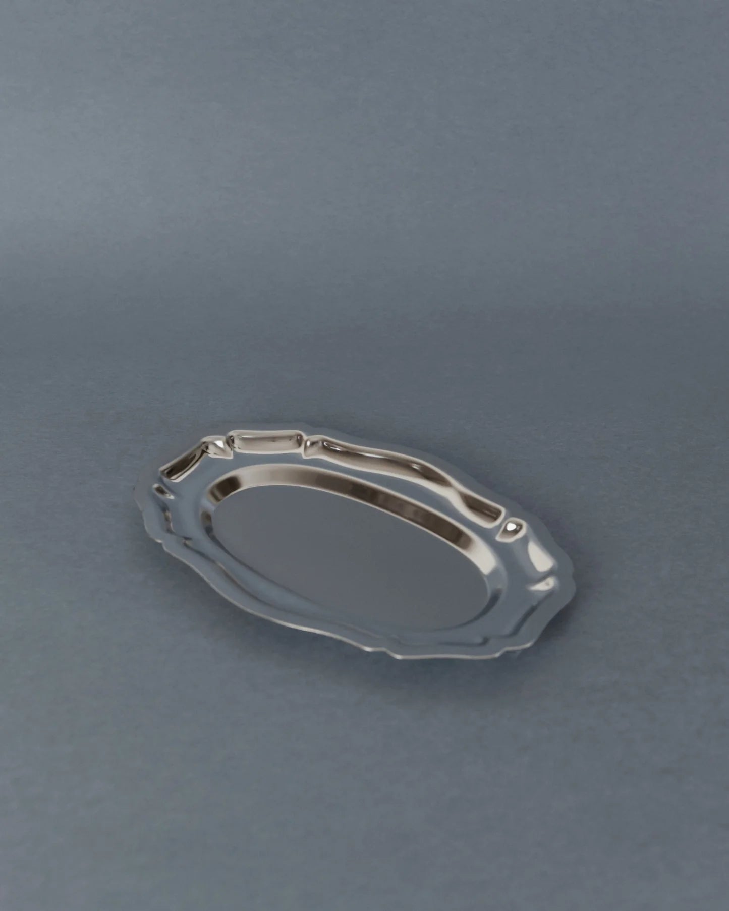 A small oval silver serving tray with a decorative wavy rim, shown on a smooth gray surface.