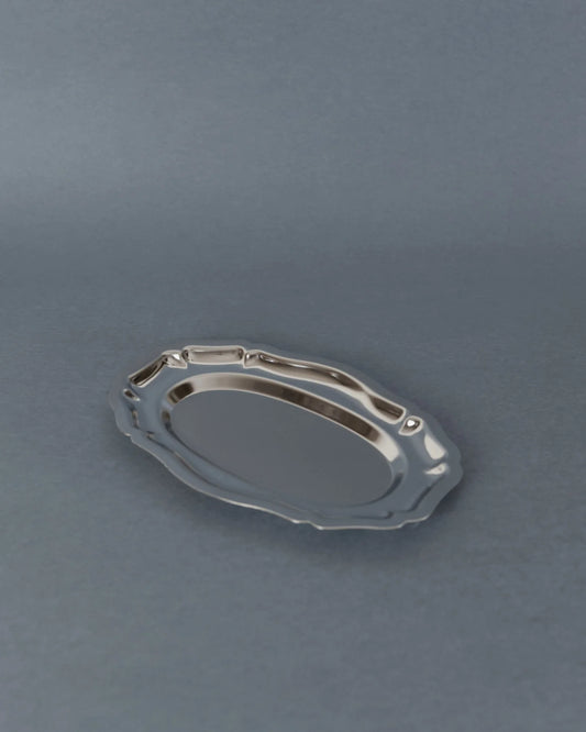 A small oval silver serving tray with a decorative wavy rim, shown on a smooth gray surface.