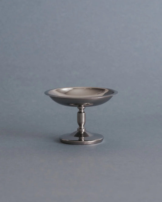 A small polished silver pedestal dish or candle holder with a flared rim, standing on a round base against a smooth gray background.