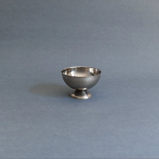 A small polished silver pedestal bowl or cup centered on a smooth slate-blue background.