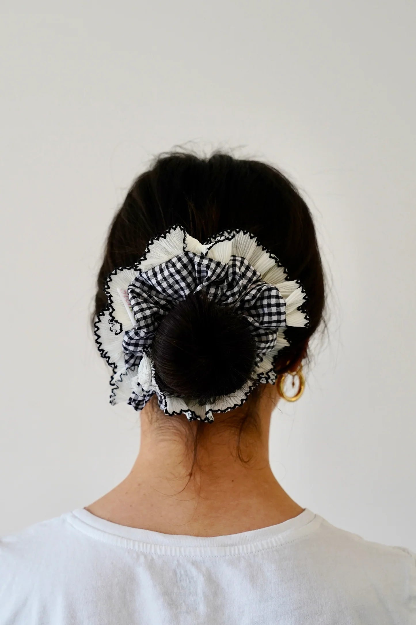 A person wearing black and white gingham large scrunchie on a white background 