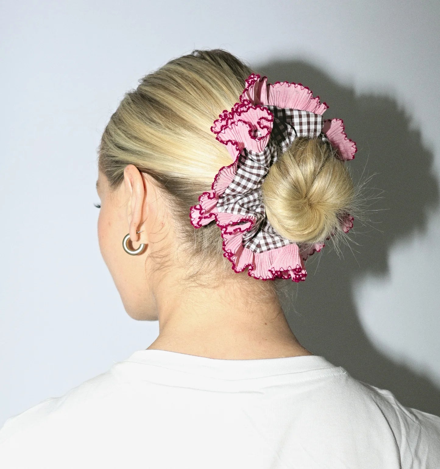 Person with a bun held up by a pink and black checkered scrunchie against a plain background