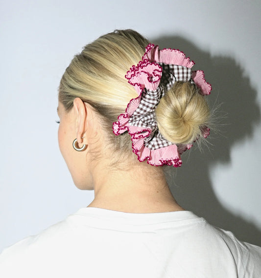 Person with a bun held up by a pink and black checkered scrunchie against a plain background