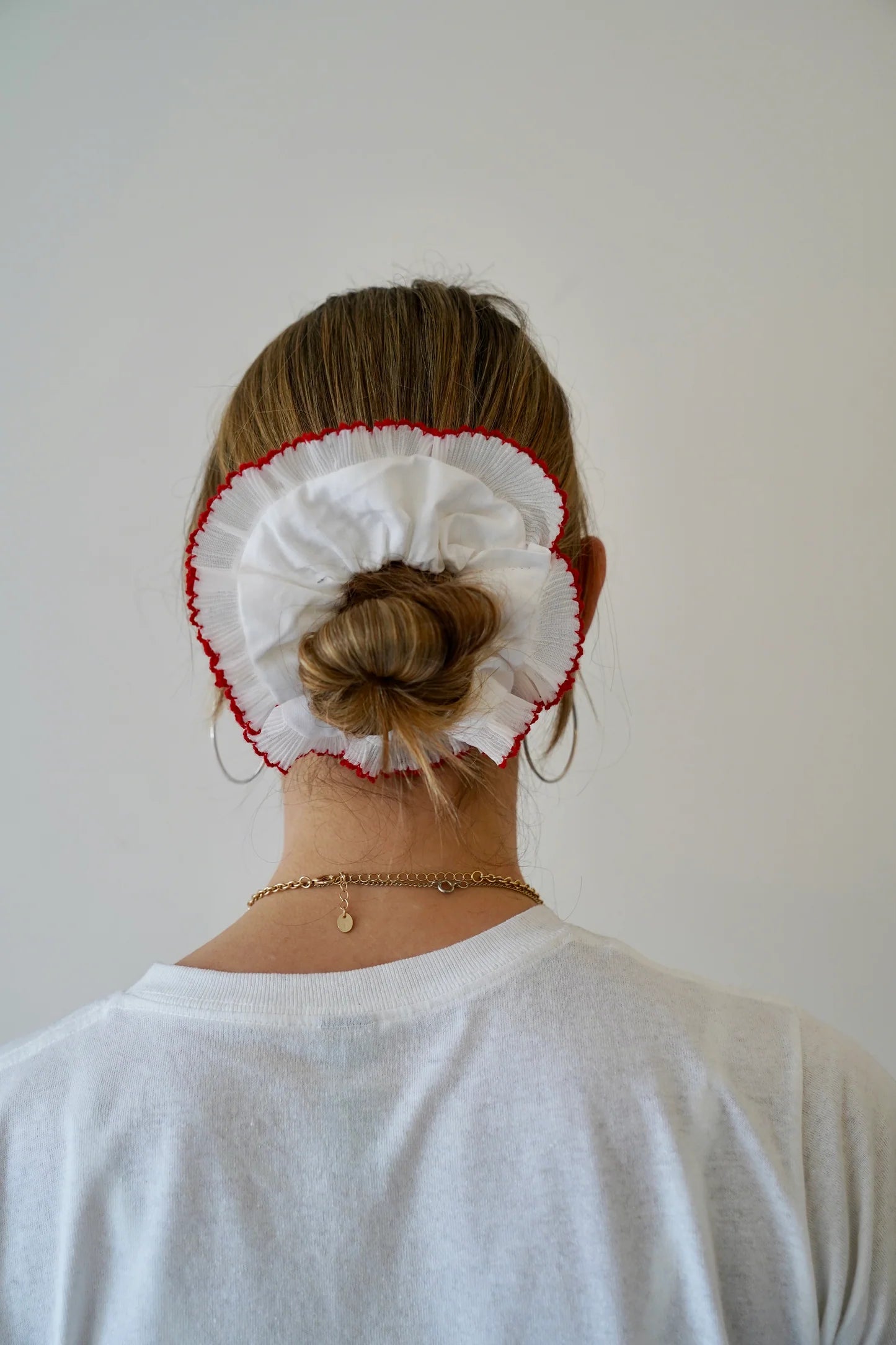 Person with a bun wearing a white headband with red trim against a plain background