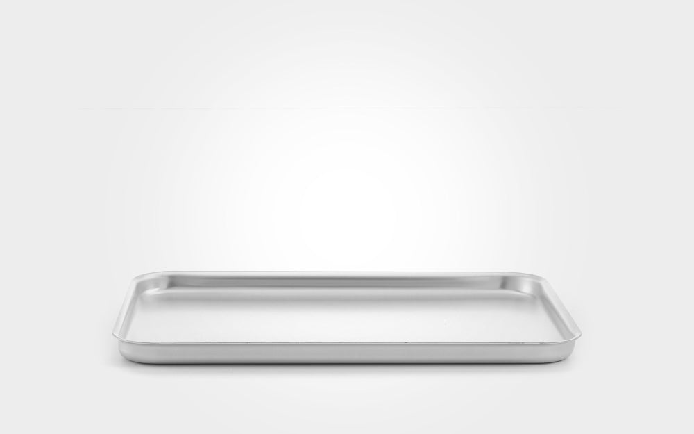 A rectangular stainless steel baking pan with raised rim and shallow depth, shown from a front angle on a light gray gradient background.