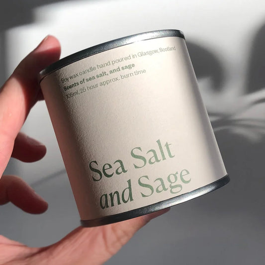 Candle container labeled 'Sea Salt and Sage' held by a hand against a neutral background