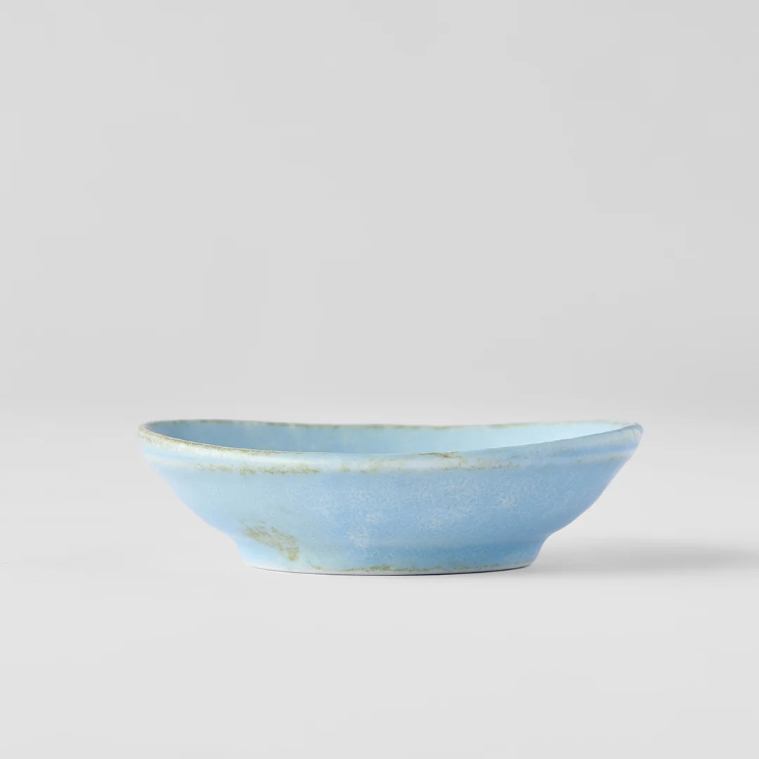 A light blue ceramic bowl with a rustic, distressed glaze showing subtle earthy tones along the rim, photographed against a neutral light gray background.