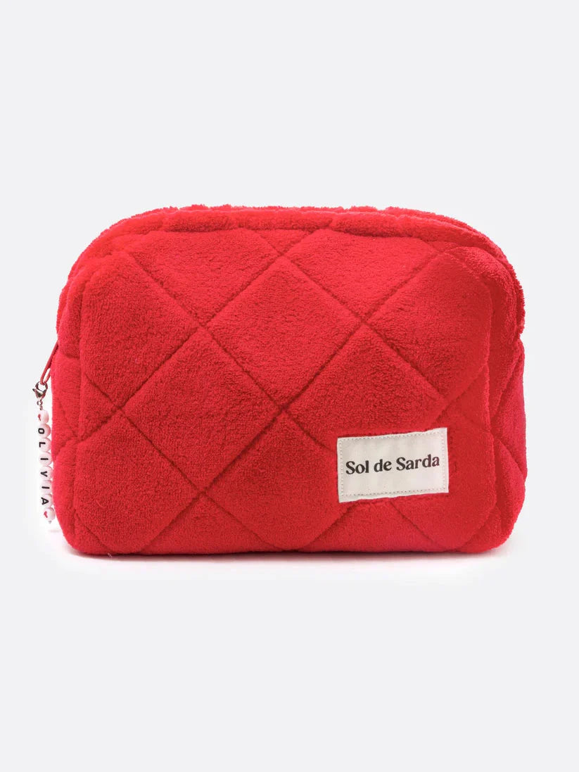 A red quilted faux fur cosmetic pouch with a white 'Sol de Sarda' brand label on the front, set against a plain light gray background.