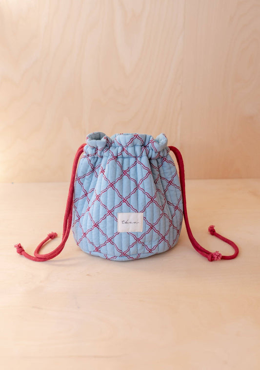 Quilted drawstring bag with red accents on a beige background